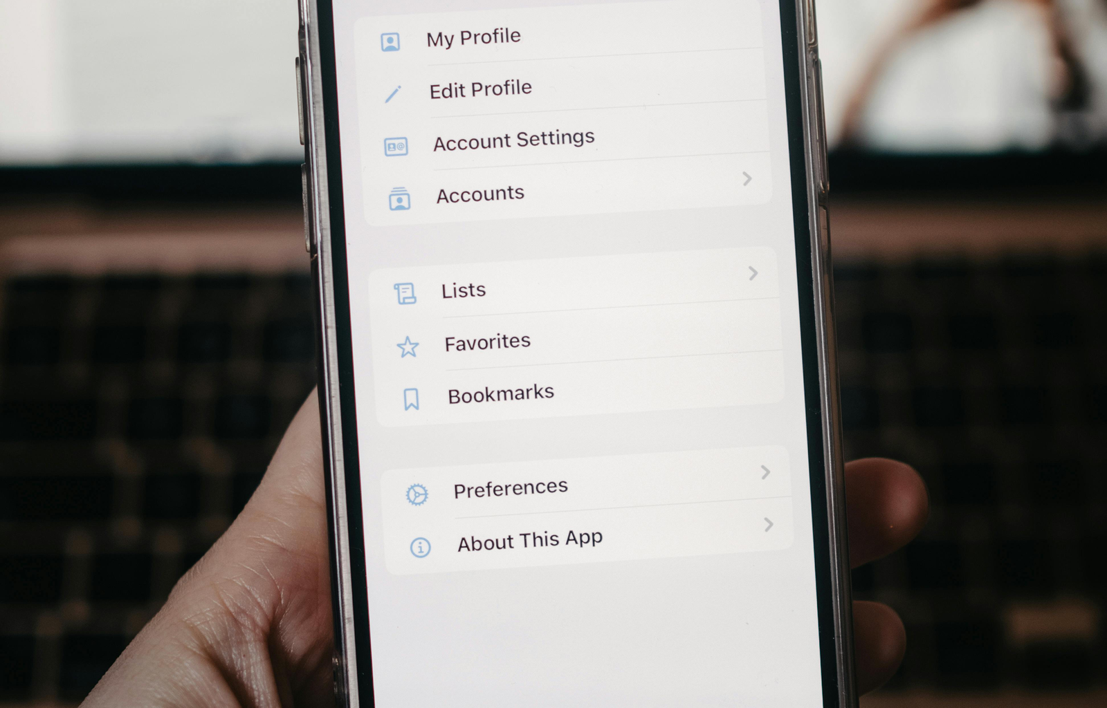 A person holds a smartphone showing the settings menu in front of a blurred background.